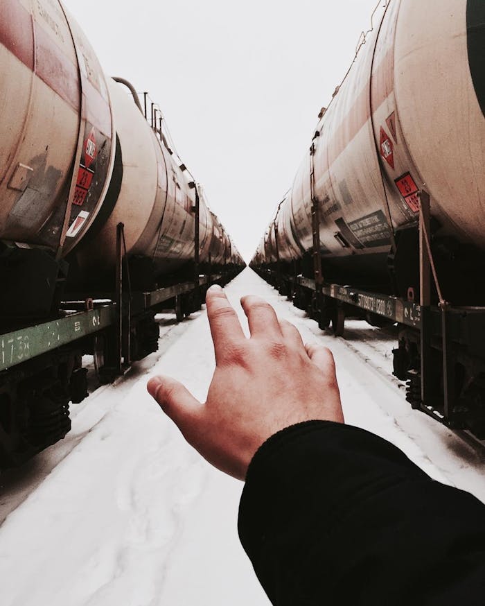 Hand extending towards long line of train tanks in snowy landscape.